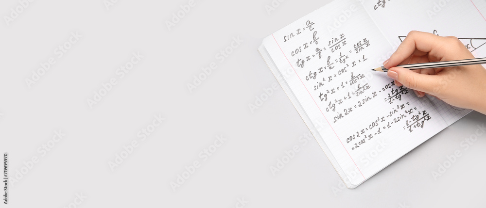 Obraz premium Woman writing maths formulas in copybook with pencil on grey background with space for text
