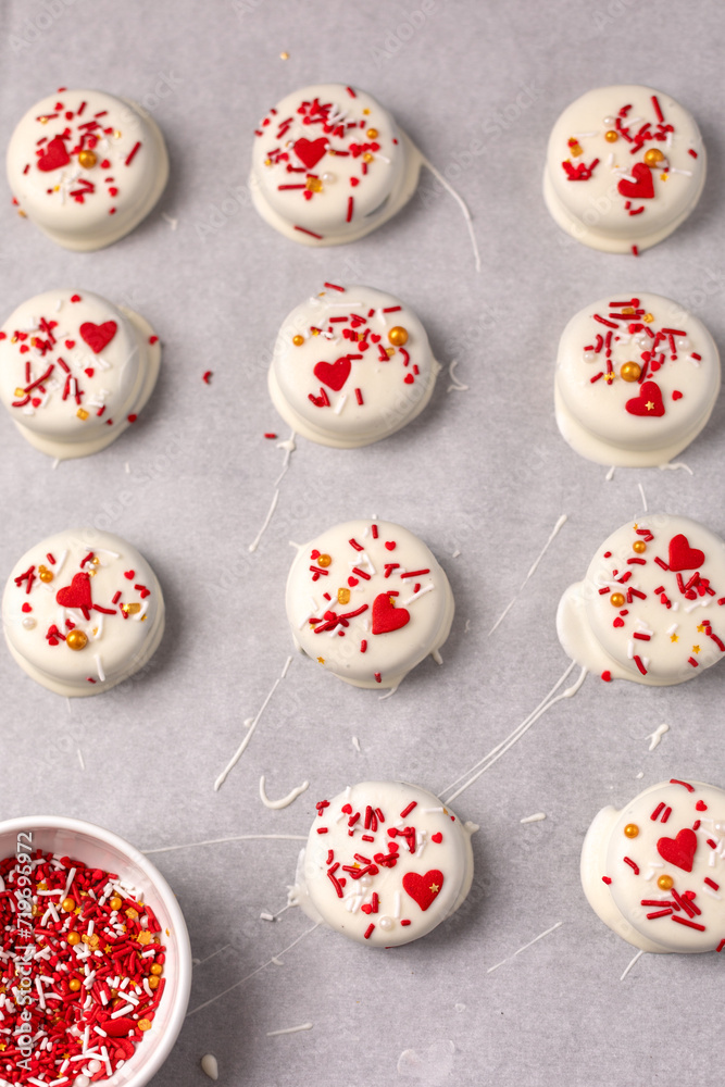 Top View of Valentine Cookies Dipped in White Chocolate and Decorated with Red, White, and Gold Sprinkles on Paarchment Paper