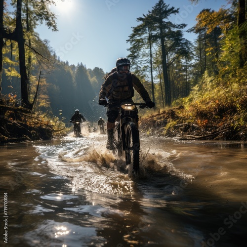 A daring group of cyclists traverse through the river on their trusty bikes, surrounded by the beautiful landscape of trees and mountains, their wheels spinning and splashing water as they conquer th
