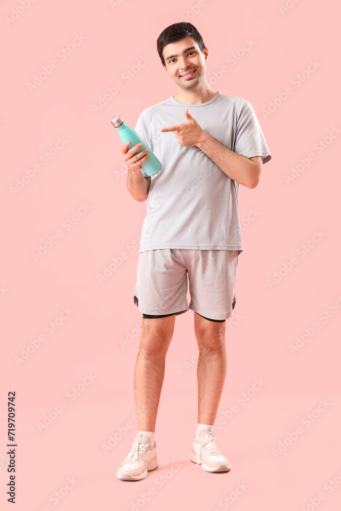 Sporty young man pointing at bottle of water on pink background