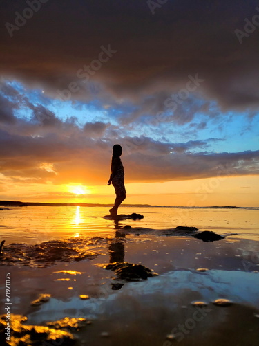a modest silhouette of a young, sweet girl, a modest, charming woman at a golden sunset, against the backdrop of a dark blue sky with blue sparkles. The silhouette is reflected in the sea water, like 