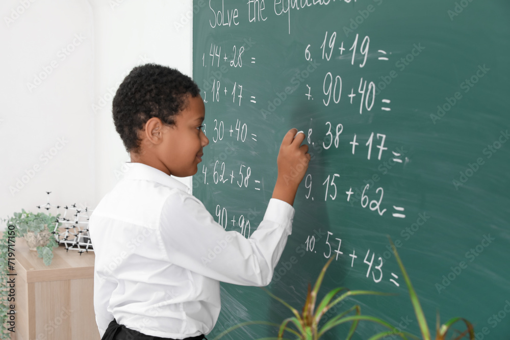 Little African-American schoolboy writing on chalkboard in classroom Little African-American schoolboy writing on chalkboard in classroom