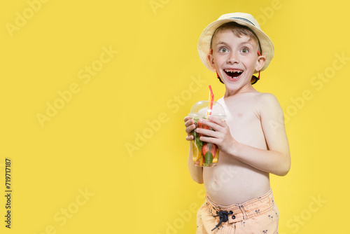 Cute little boy with inflatable ring and cocktail glass on yellow background