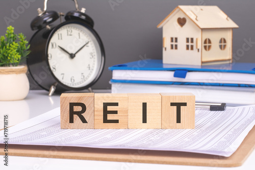reit word in wooden blocks with small wooden house and alarm clock on gray background. symbolizes the timely payment of membership fees.