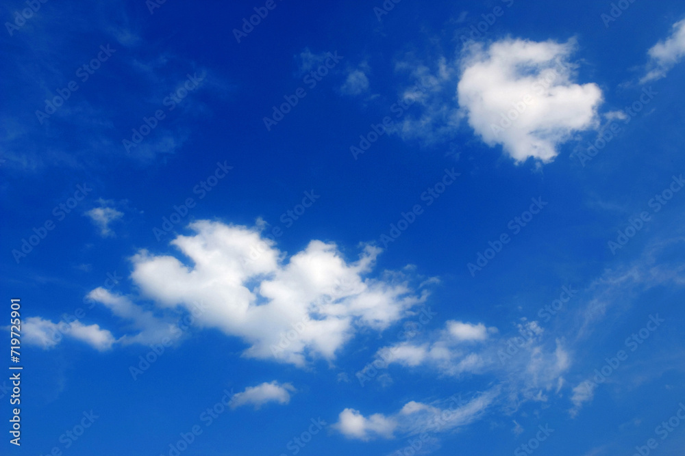 two white fair weather clouds, cumulus in the blue sky
