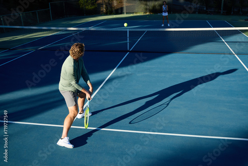 A tennis player hitting balls on a shadowy tennis court
