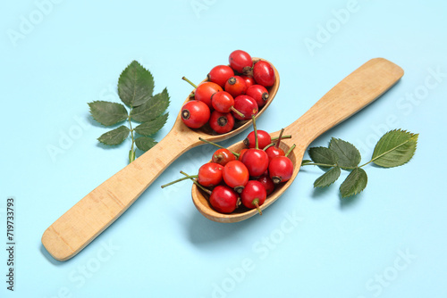 Wooden spoons with fresh rose hip berries and leaves on blue background © Pixel-Shot