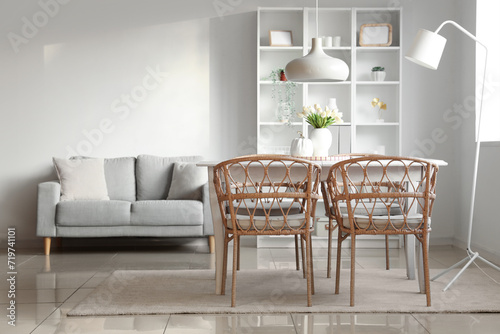 Interior of light living room with tulip flowers on dining table and cozy grey sofa