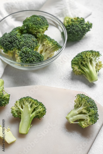 Glass bowl and board with fresh broccoli cabbages on white background