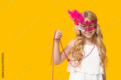 Adorable little girl wearing carnival mask on yellow background photo
