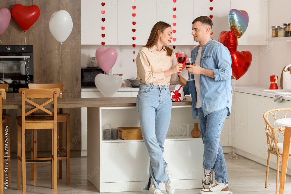 Fototapeta premium Beautiful young couple drinking wine and celebrating Valentine's Day in kitchen at home