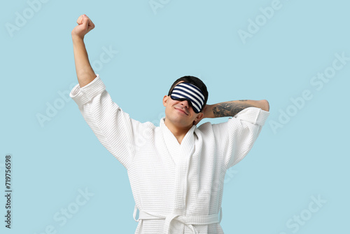 Portrait of handsome young man in bathrobe and sleeping mask on blue background © Pixel-Shot