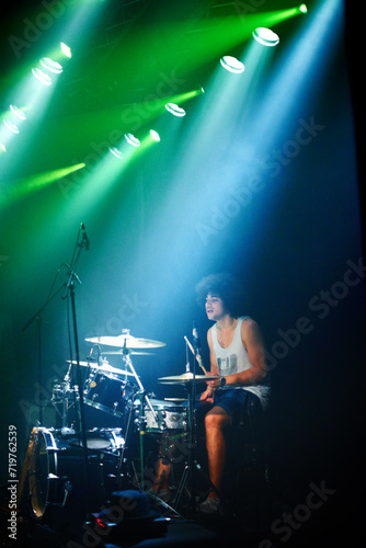 Music festival, drums and man with instrument by stage and playing in color spotlight at night. Young person, creative drummer and talented musician in band for disco sound and performance at event