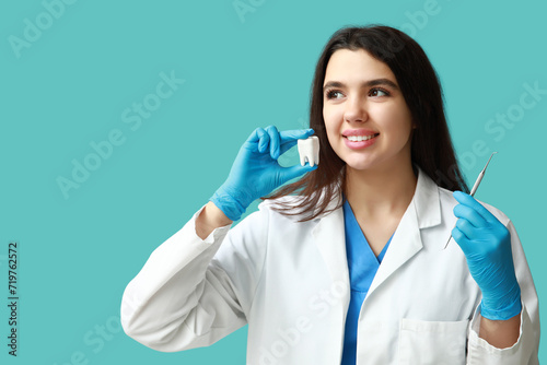 Female dentist with tool and plastic tooth on blue background. World Dentist Day