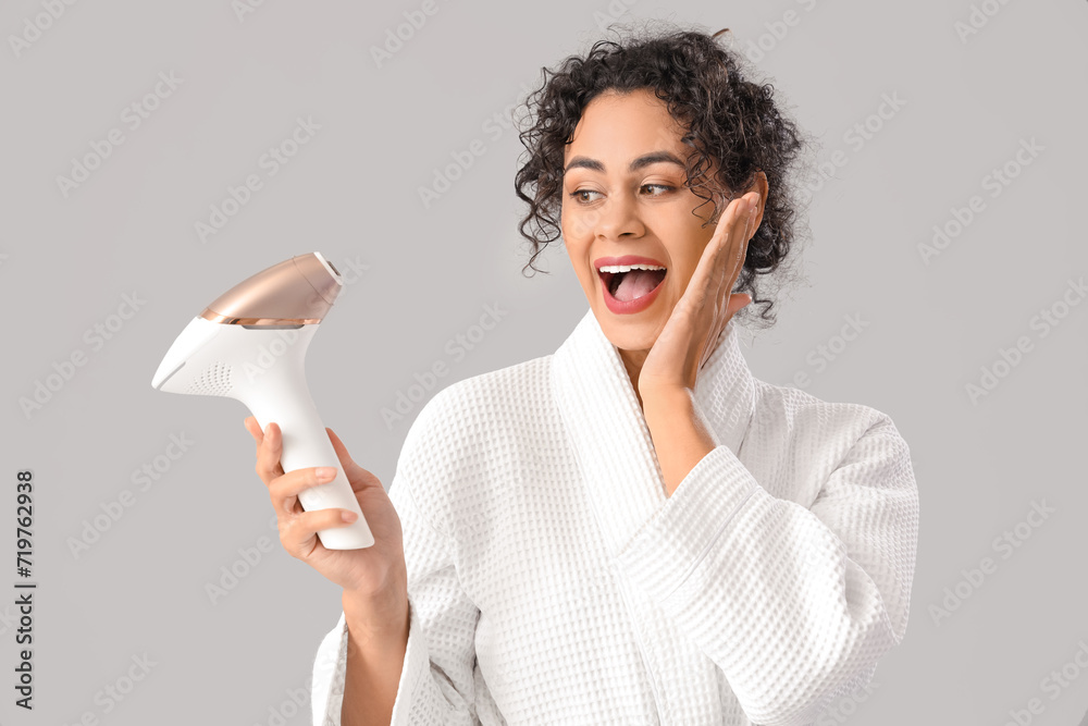Beautiful surprised African-American woman with photoepilator on grey background Beautiful surprised African-American woman with photoepilator on grey background
