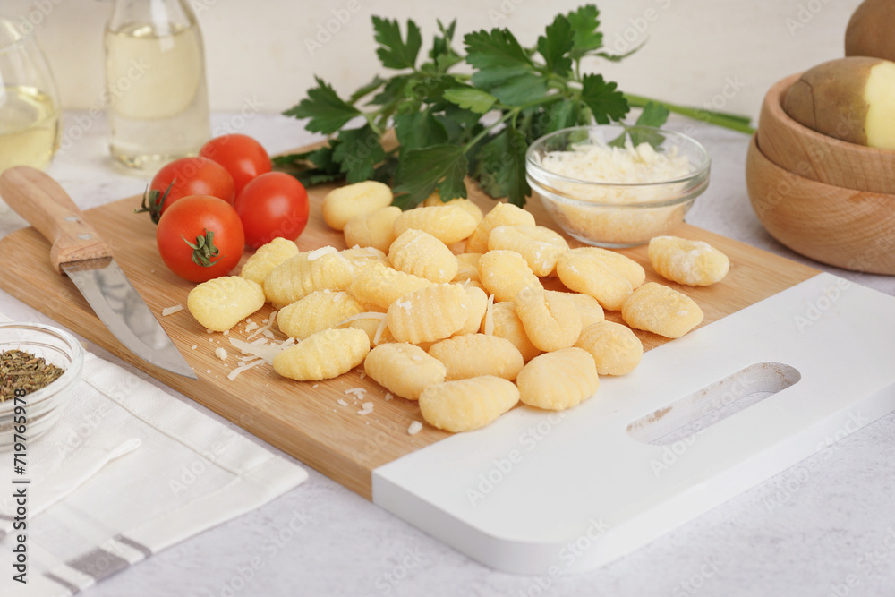 Wooden board with tasty gnocchi, tomatoes, parsley and grated cheese on light background, closeup Wooden board with tasty gnocchi, tomatoes, parsley and grated cheese on light background, closeup