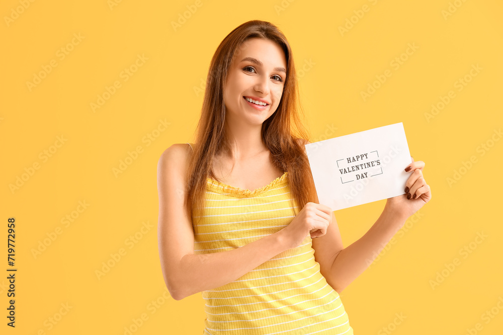 Beautiful young woman holding greeting card with text HAPPY VALENTINE'S DAY on yellow background Beautiful young woman holding greeting card with text HAPPY VALENTINE'S DAY on yellow background