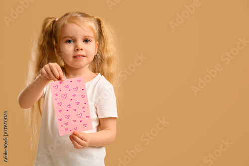 Cute little girl holding greeting card with hearts on beige background. Valentine's Day celebration