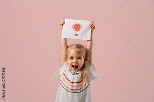 Emotional little girl holding greeting card with text I LOVE YOU on pink background. Valentine's Day celebration