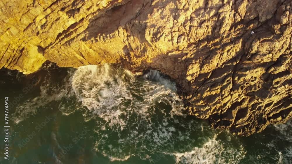 Waves crashing cliffs on sunny evening, aerial downwards view Waves crashing cliffs on sunny evening, aerial downwards view