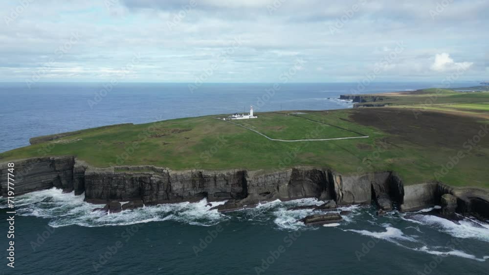 Loophead lighthouse on rugged cliffs with waves crashing, cloudy sky, aerial view Loophead lighthouse on rugged cliffs with waves crashing, cloudy sky, aerial view