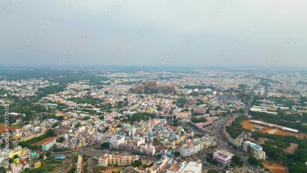 The bustling cityscape of Tiruchirappalli with dense buildings and roads and Malaikottai Rock Fort in the background. Daylight, aerial view. Tamil Nadu, India The bustling cityscape of Tiruchirappalli with dense buildings and roads and Malaikottai Rock Fort in the background. Daylight, aerial view. Tamil Nadu, India