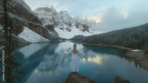 Mystery woman raising arm in front of calm lake with mountain reflection photo