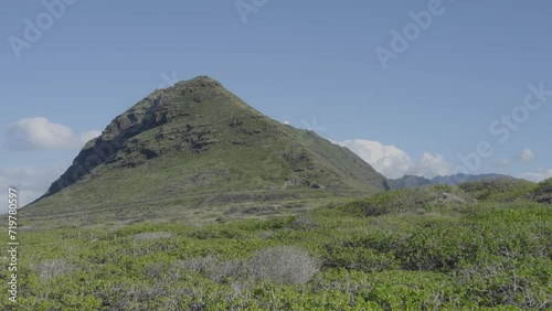 stationary shot of a pointed volcanic mountain on Oahu Hawaii with green lush filds in the foreground and blu sky behind photo