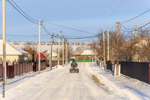 A man on an ATV rides through the village in winter. Background with selective focus and copy space