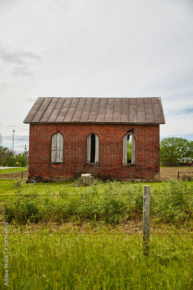 Abandoned Red Brick Rural Building with Overgrown Grass and Overcast Sky Abandoned Red Brick Rural Building with Overgrown Grass and Overcast Sky