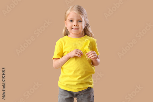 Cute little girl with yellow ribbon on brown background. Childhood cancer awareness concept