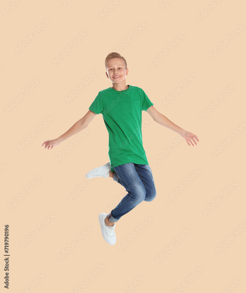 Teenage boy jumping on beige background, full length portrait