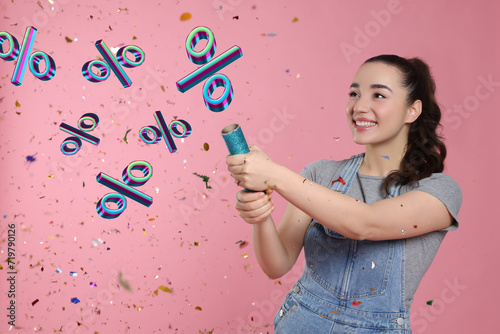 Discount offer. Happy young woman blowing up party popper on pink background. Confetti and percent signs in air