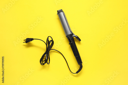 Curling iron on yellow background, top view