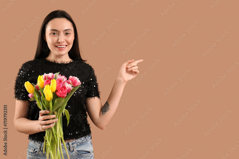 Young woman with bouquet of beautiful tulips pointing at something on brown background. International Women's Day