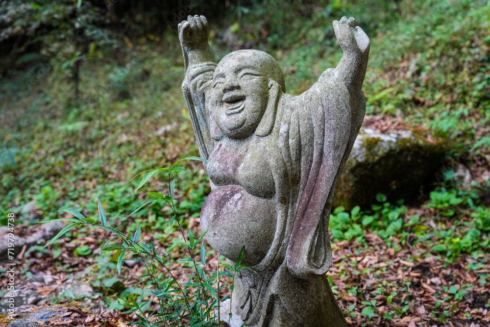 Moss covered stone Buddhist monk carving with arms raised Moss covered stone Buddhist monk carving with arms raised