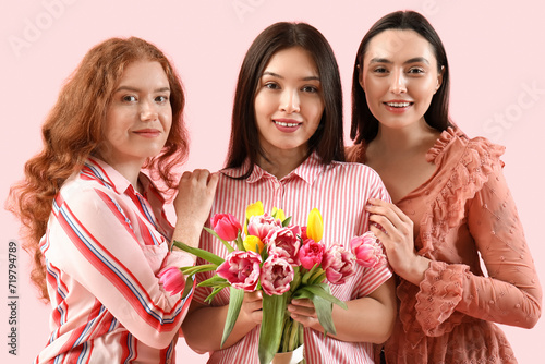 Young women with bouquet of beautiful tulips on pink background. International Women's Day