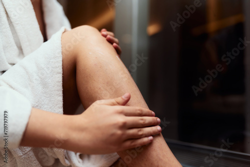 A woman indulges in her self care routine, pampering her skin after a relaxing bath by applying hydrating cream to her legs, embracing the essence of beauty and well being