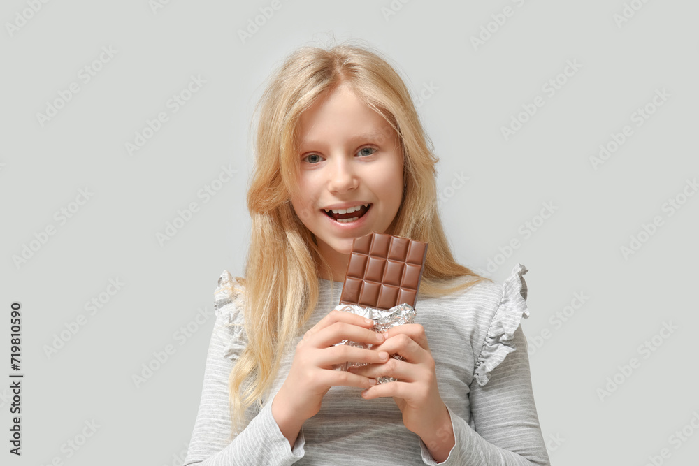 Cute little girl with sweet chocolate bar on grey background Cute little girl with sweet chocolate bar on grey background