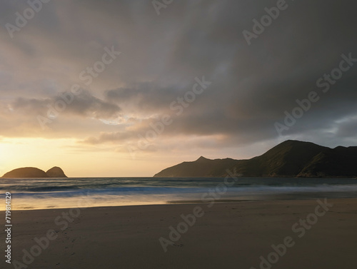 A serene beach at dusk, with gentle waves lapping the shore and dark clouds overhead, illuminated by the fading sunlight.