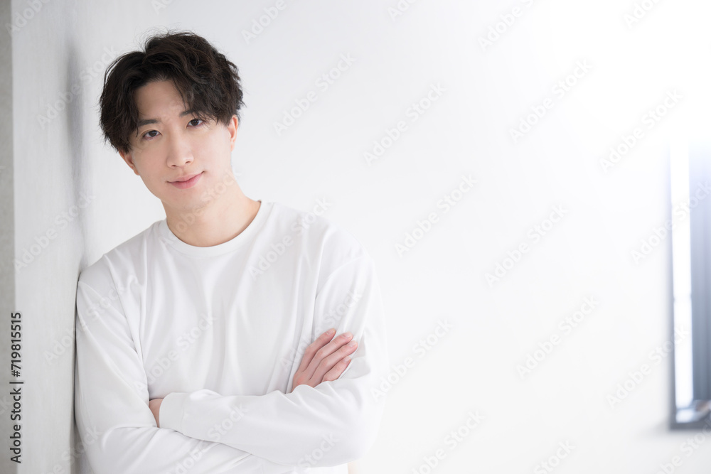 Young handsome Asian (Japanese) man leaning against a wall and folding his arms Young handsome Asian (Japanese) man leaning against a wall and folding his arms