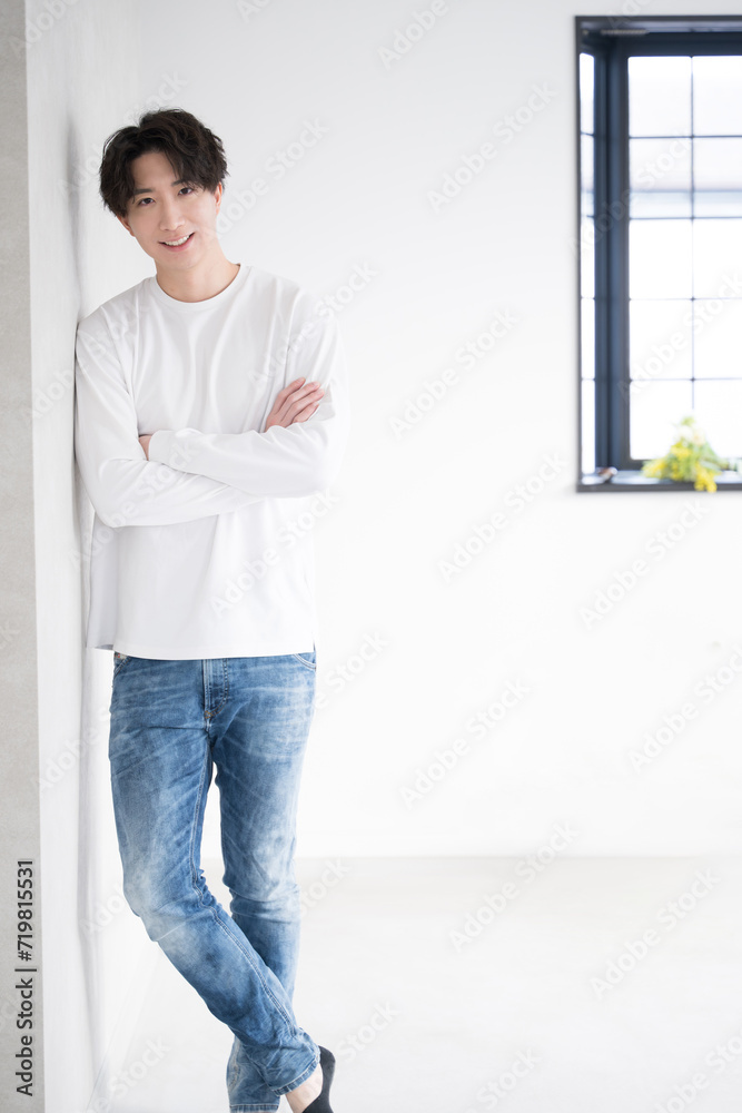 Vertical view of a young handsome Asian (Japanese) man leaning against a wall and folding his arms Vertical view of a young handsome Asian (Japanese) man leaning against a wall and folding his arms
