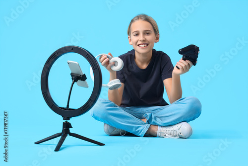 Teenage blogger with game pad and headphones recording video on blue background