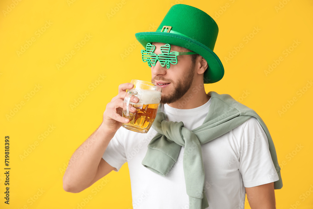 Young man in leprechaun hat and decorative glasses in shape of clover with glass of beer on yellow background. St. Patrick's Day celebration Young man in leprechaun hat and decorative glasses in shape of clover with glass of beer on yellow background. St. Patrick's Day celebration