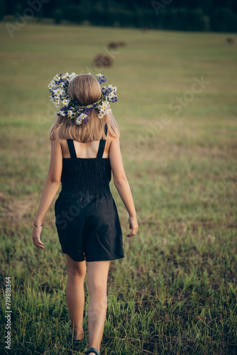 a girl with blond hair and a wreath of flowers on her head walks through the fields in summer