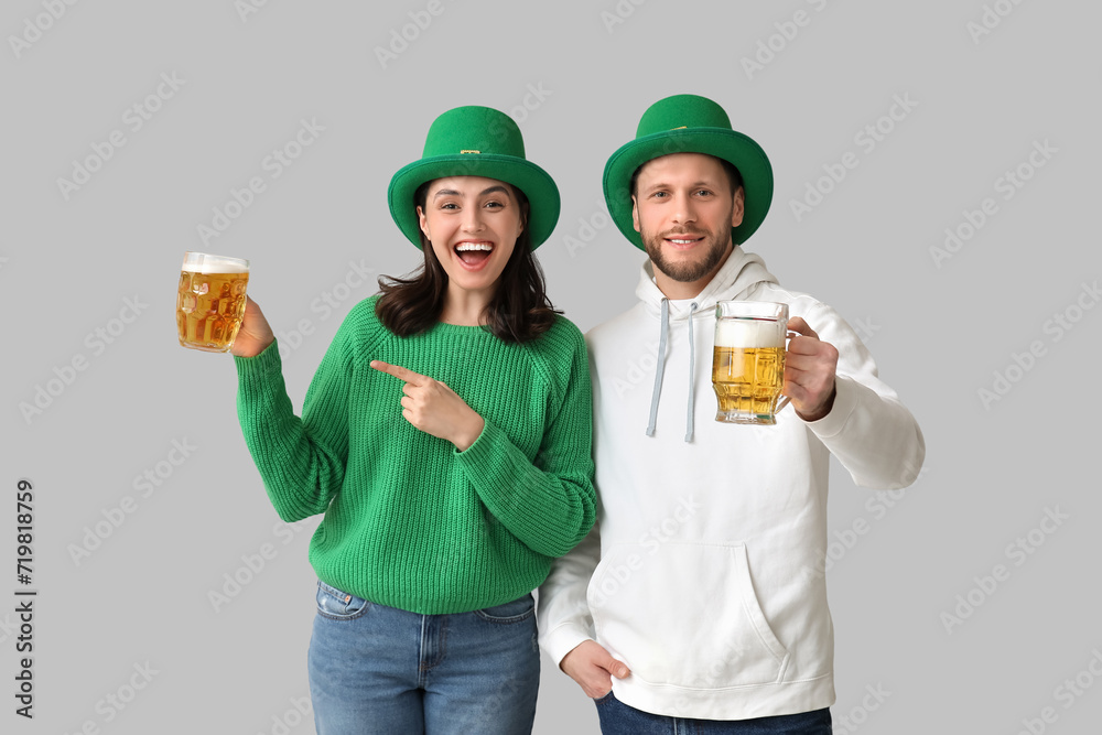 Beautiful young couple in leprechaun hats pointing at glasses of beer on grey background. St. Patrick's Day celebration Beautiful young couple in leprechaun hats pointing at glasses of beer on grey background. St. Patrick's Day celebration