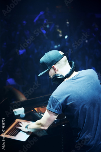 Concert, DJ and man with mixing music by stage and laptop in color spotlight with large crowd. Young person, creative and talented musician in band for sound and performance at event on night club
