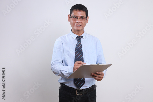Happy adult Asian businessman in glasses holding clipboard and looking at camera