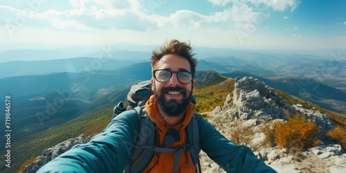 Hiker man reaches the summit of a mountain, capturing the triumphant moment by taking a selfie portrait. Convey the joy and accomplishment in his expression as he smiles at the camera
