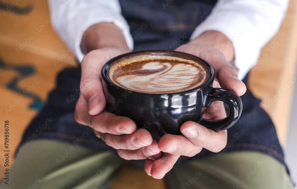 Close up barista hands holding a cup of latte art coffee in coffee shop